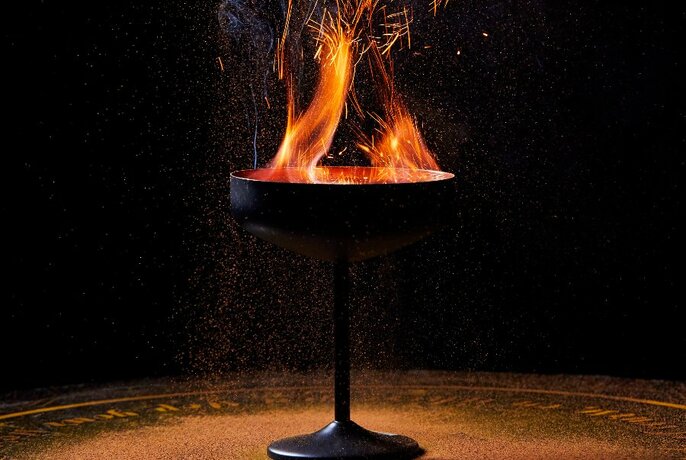 A black cocktail glass holding a burning drink on a tray.