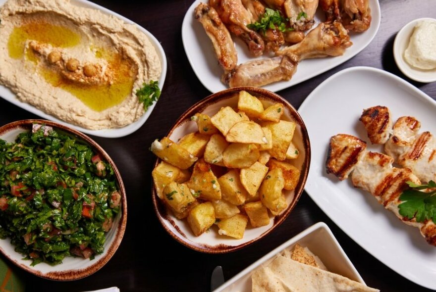 A spread of food including potatoes, chicken, and hummus. 