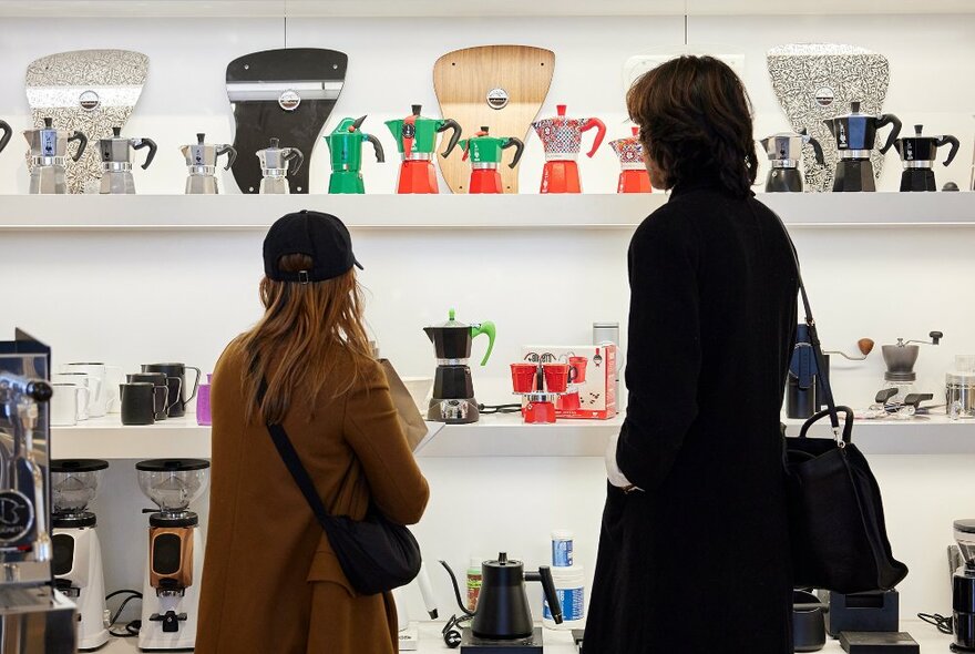 Two people looking at a display of colourful coffee pots.
