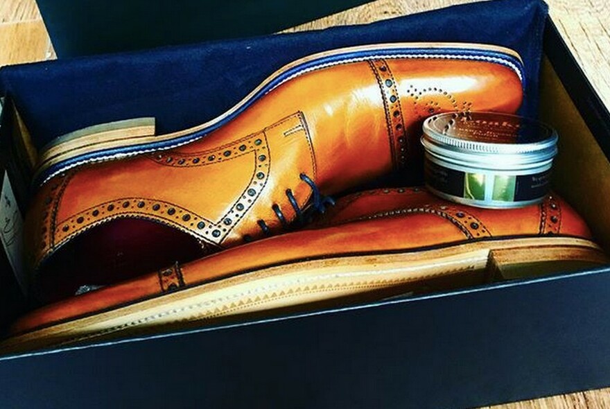Shoebox with a pair of men's light brown leather brogues and jar of shoe polish.