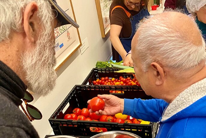 Two older men looking at crates of tomatoes, one picking a tomato up for a closer look. 