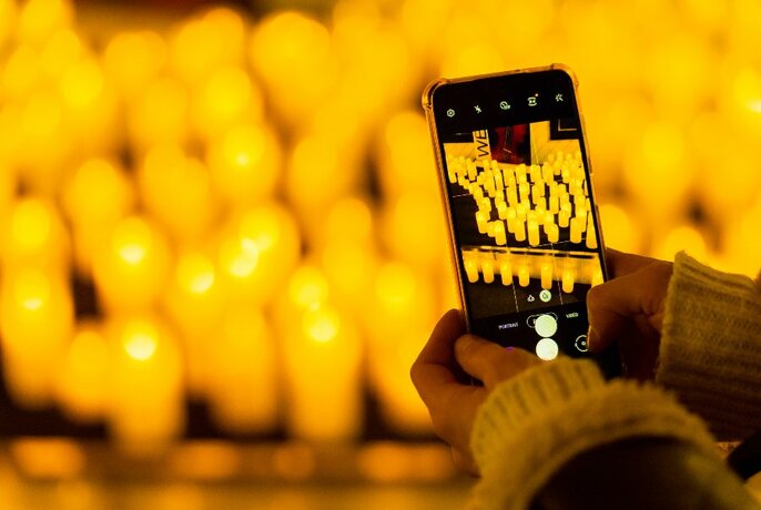 Hands holding a mobile phone in front of an array of yellow candles.