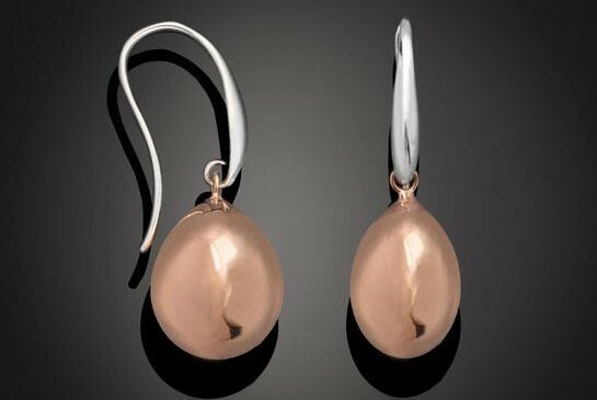 Rose pink pearl drop earrings with a curled silver fitting, against a dark background.