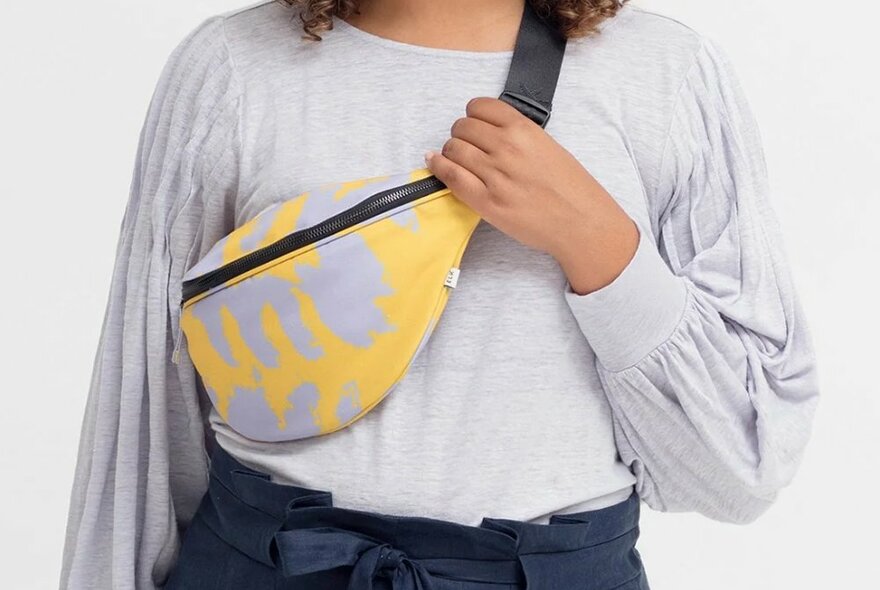 A model wearing a yellow and grey bumbag across her body.