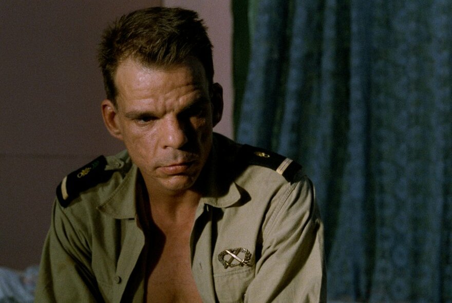 Film still of an actor wearing an open military shirt, looking concerned.