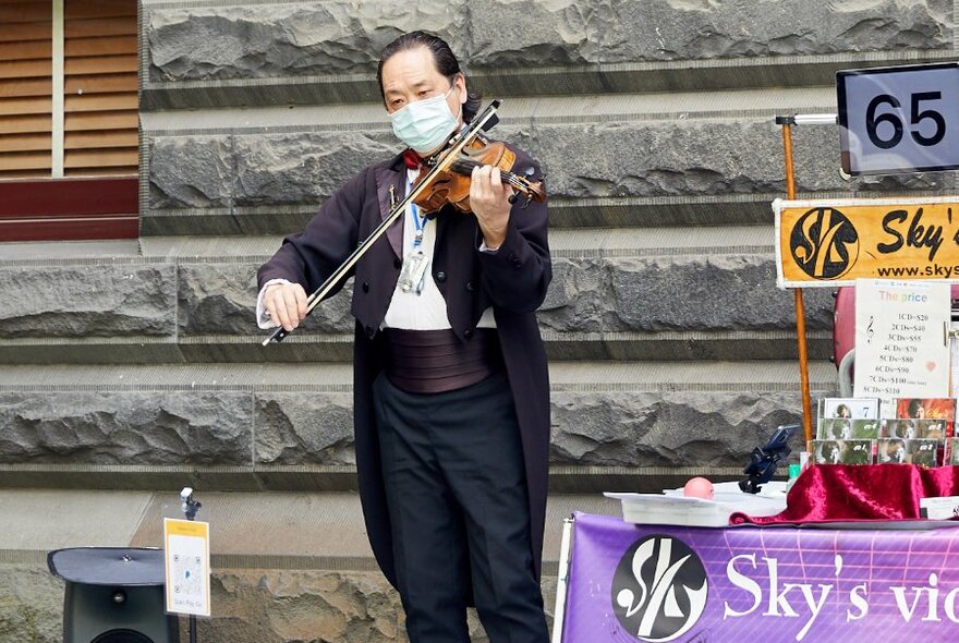 A violinist busker wearing a tuxedo.