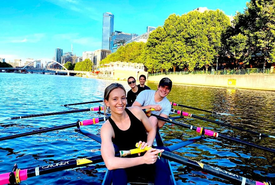 Four smiling people posing in a row boat on the Yarra River.
