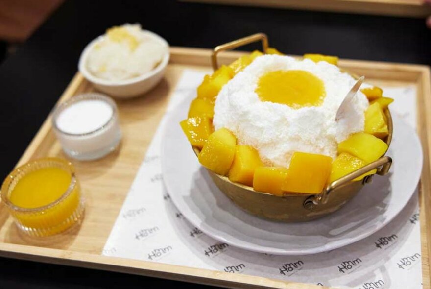 A shaved ice and mango dessert on a wooden tray