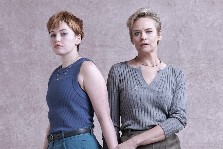 Two women, one looking worried and the other serious, against a speckled neutral background. 