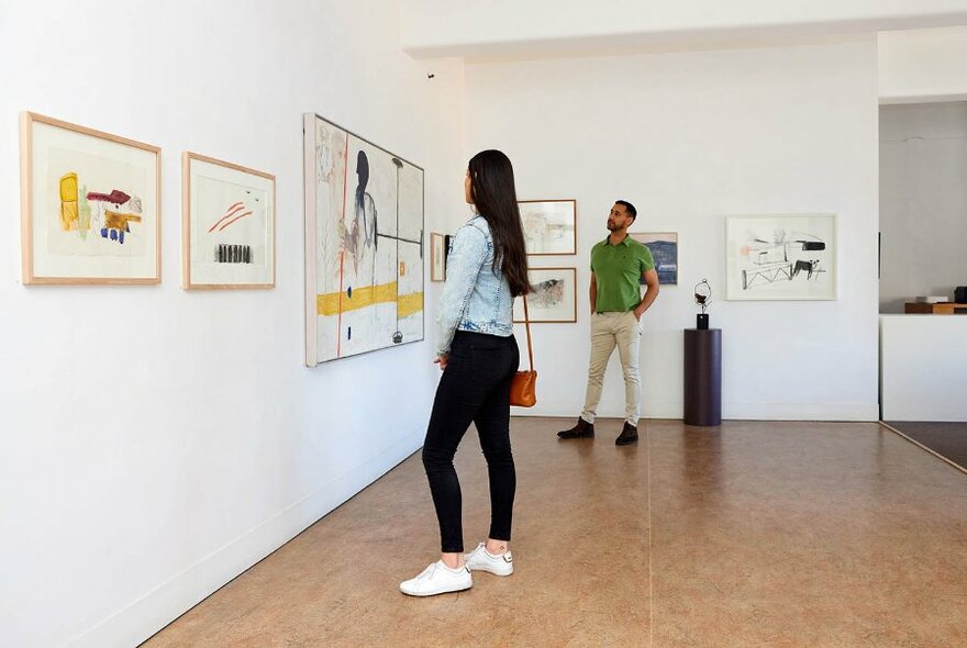 Two people looking at artworks on white gallery walls.