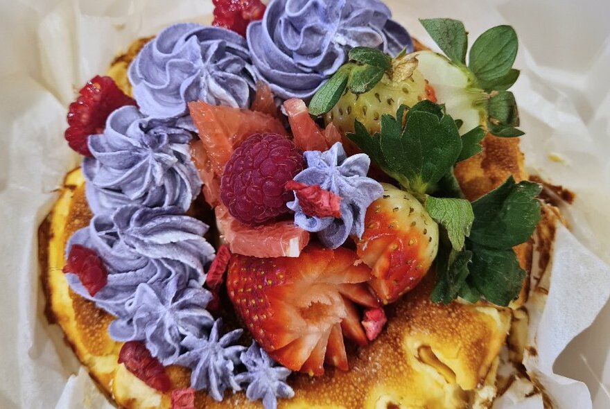 Strawberries, raspberries and piped purple icing on top of stack of pancakes. 
