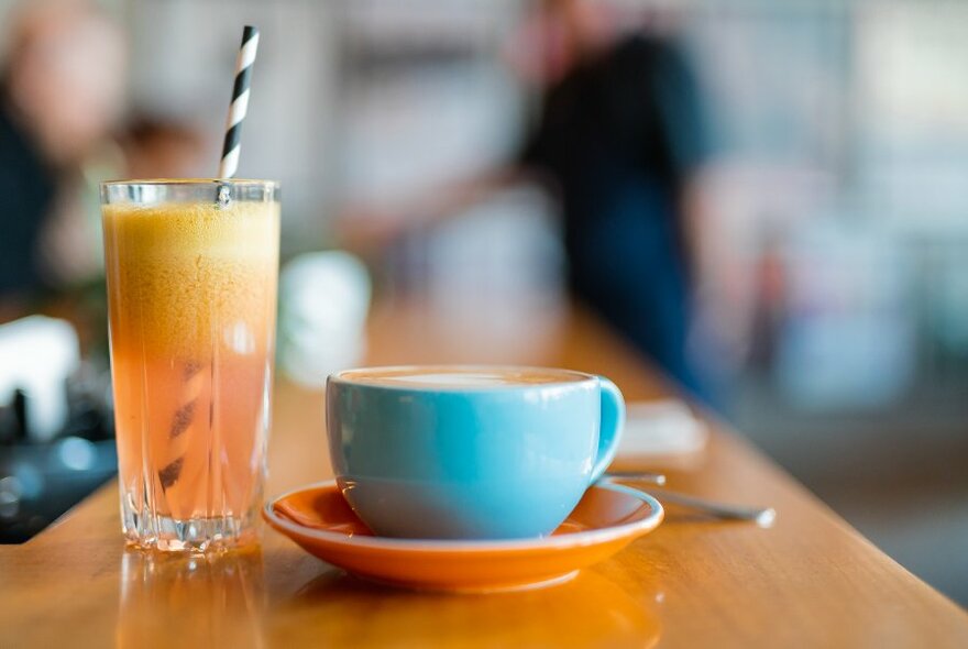 A glass of orange soft drink with a stripy straw and a cup of coffee