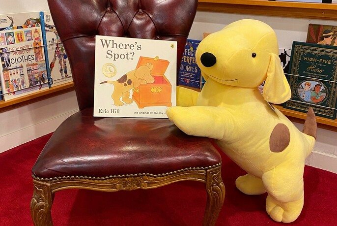 Children's picture book 'Where's Spot?' on a red armchair with Spot, a soft toy dog placed alongside.