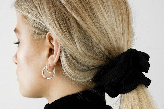 Ponytailed model wearing two gold hoop earrings.
