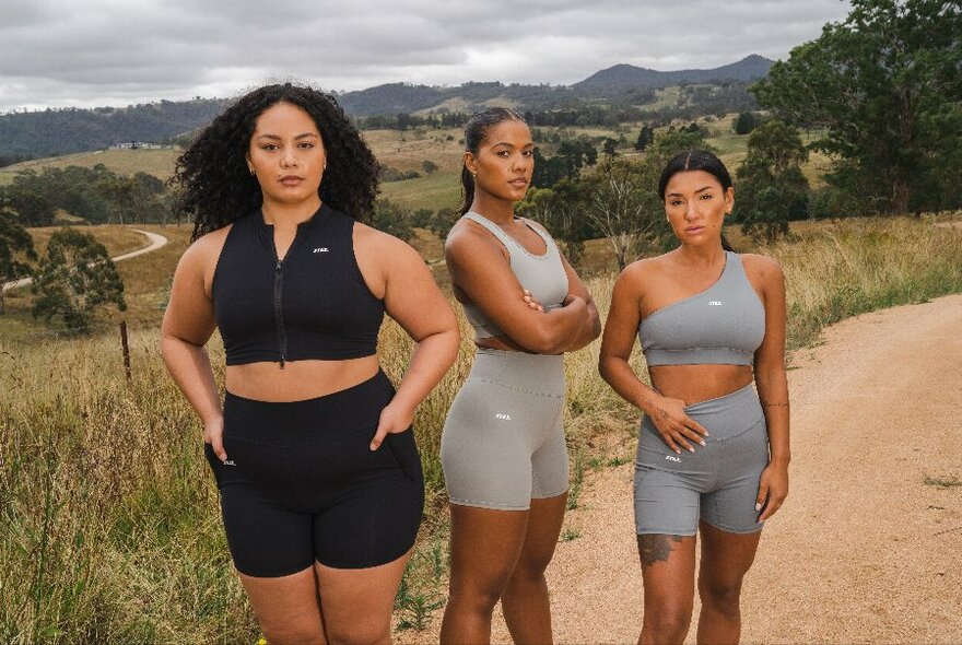 Three women wearing lycra shorts and tops, standing outside in a mountain landscape.