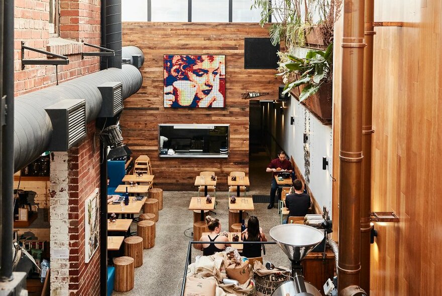 View from above of people dining in a cafe with high ceilings, timber walls and artwork.