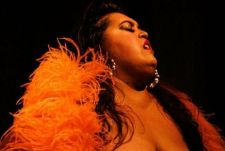 Cabaret dancer wearing orange feathers and large earrings, in profile.