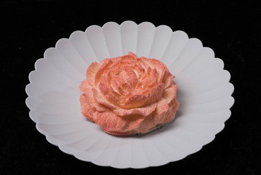 A rosette shaped cake in the middle of a fringed while plate.