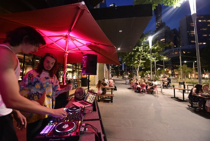 Two DJs under pink-lit umbrella in Melbourne Recital Centre forecourt.