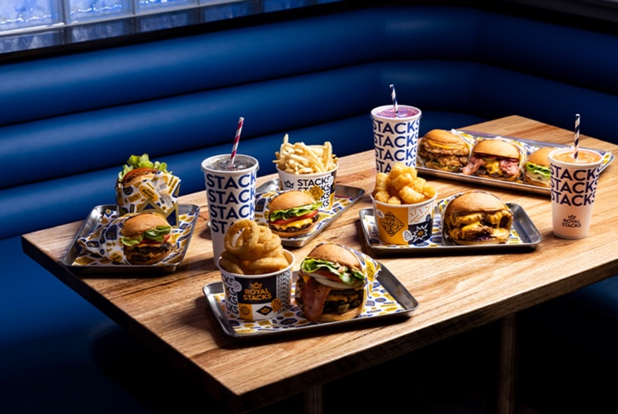 Trays of chips, burgers and shakes on a wooden table next to a blue bench seat.