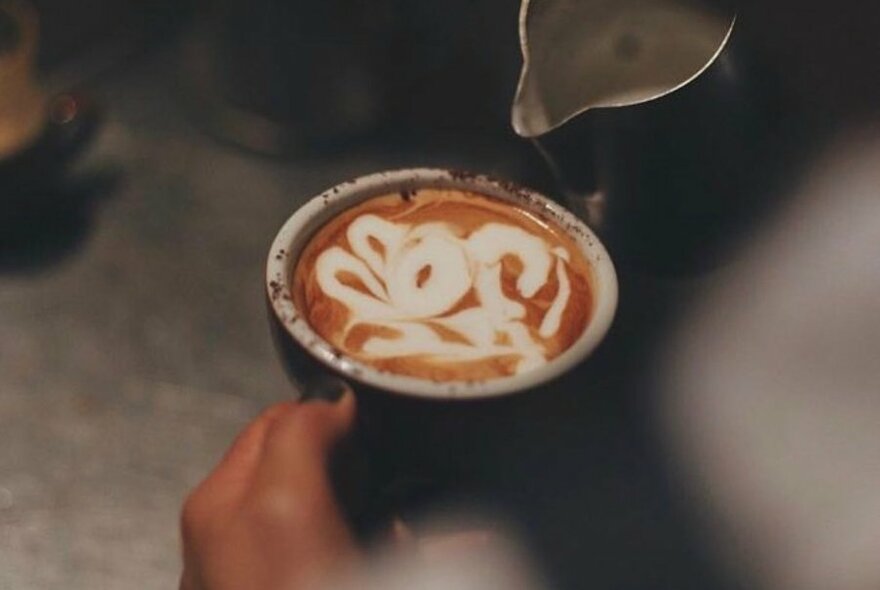 A barista's hands performing latte art on a cup of coffee.