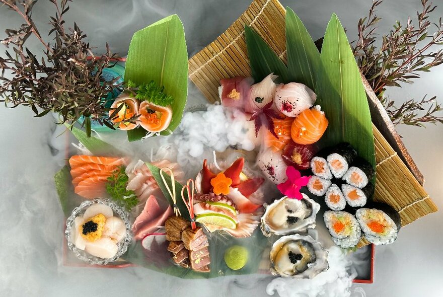 Overhead view of a platter of food that includes sushi, sashimi, shucked oysters and other fish.