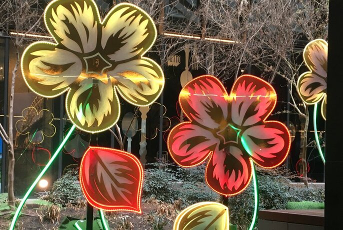 An illuminated garden installation featuring tall yellow and red flowers.