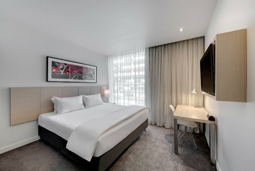 Hotel room with large white bed, cream details and grey carpet.