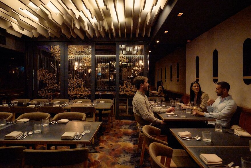 Three people dining in a sophisticated dimly lit restaurant.