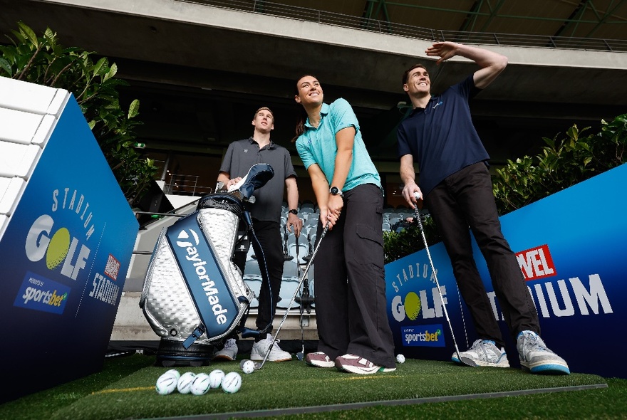 Three people teeing off on a synthetic grass surface, each with golf clubs in hand.