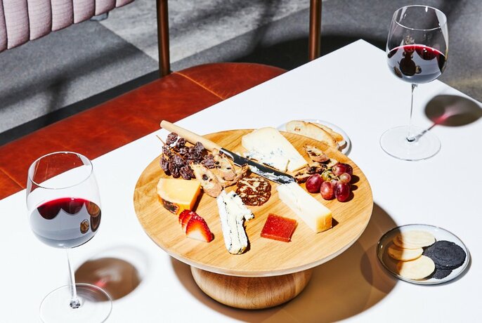 Antipasti board of cheese, grapes, and crackers on a table with two glasses of red wine.