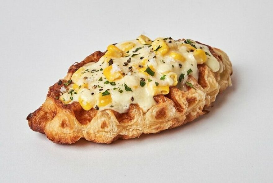 A savoury croffle, a cross between a waffle and a croissant, covered in melted cheese and corn kernels.
