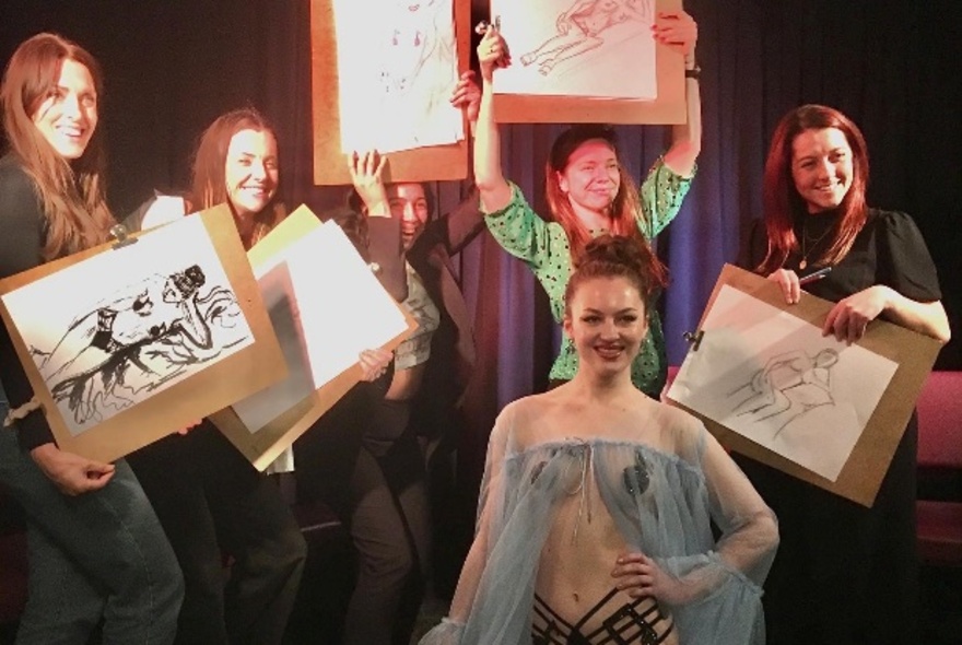 A group holding up pieces of artwork they have drawn, with a performer posing.