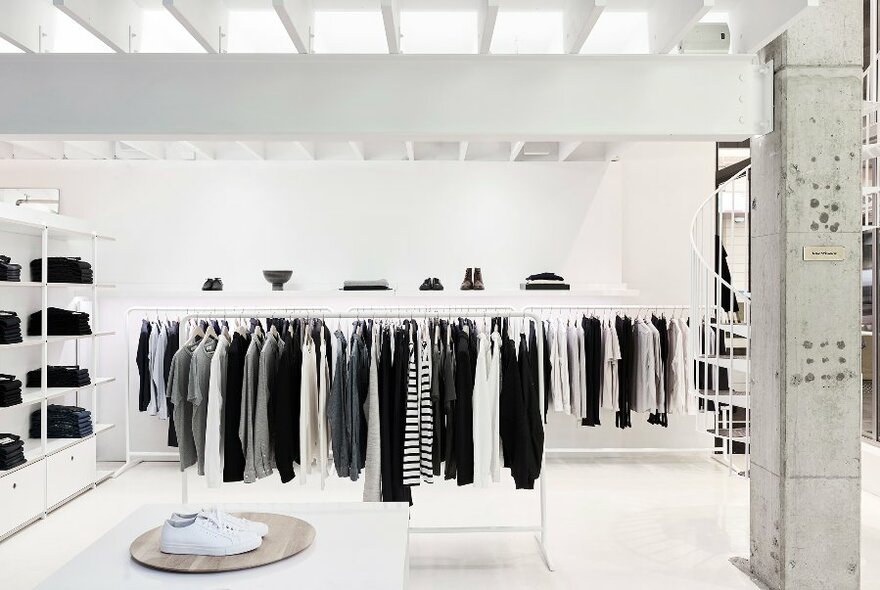 Interior of a fashion store, white walls and fittings, sleek and contemporary with racks of black and white clothes and accessories and a minimalist design.