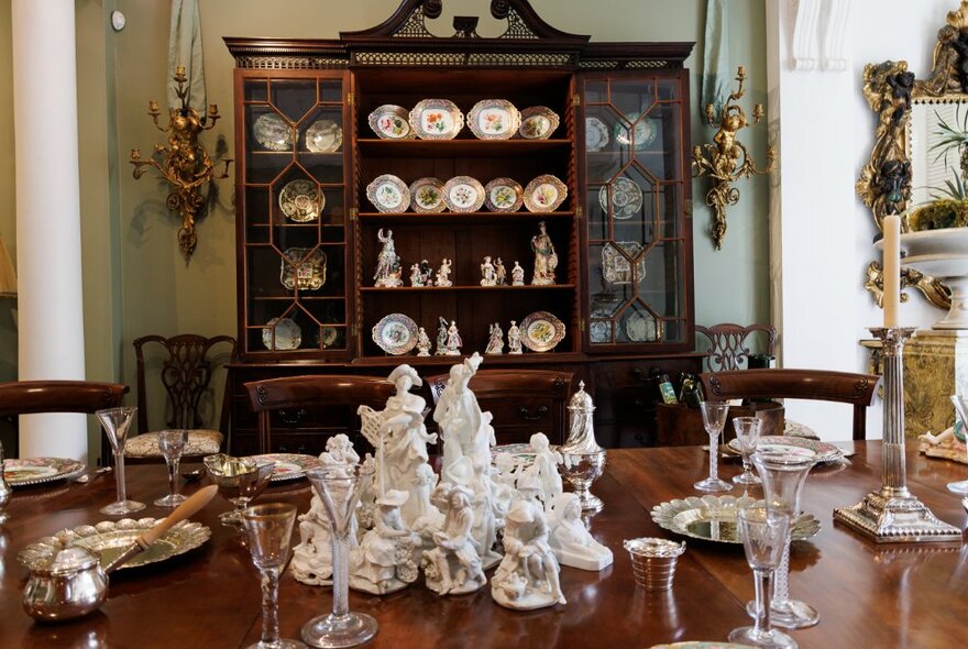 Interior room of The Johnston Collection house museum, showing decorative porcelain and glassware arranged on a dining table, a china display cabinet against the rear wall.