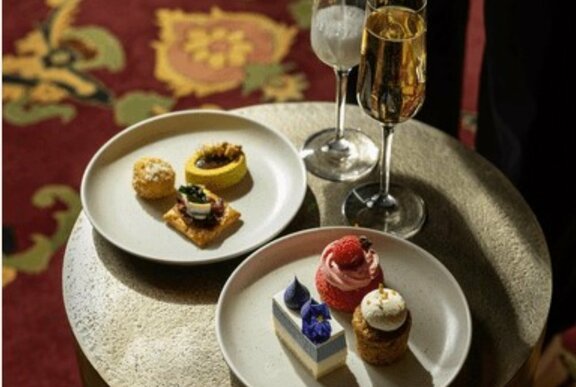 Two plates of high tea food offerings, alongside two glasses of sparkling wine, on a small round table.