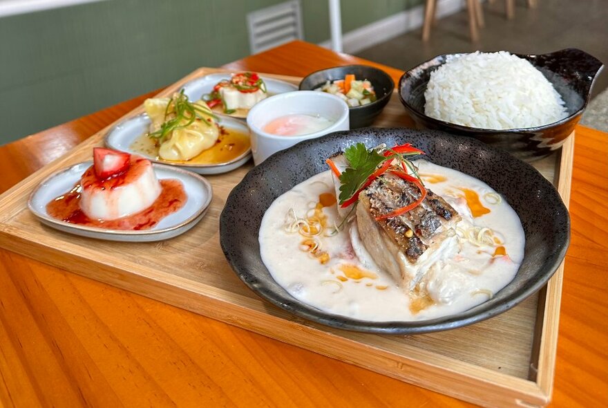 Dishes including rice and condiments on a wooden tray.