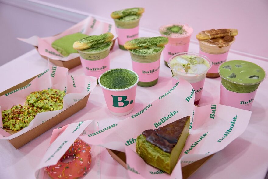 A selection of green matcha drinks and cakes in pink packaging.