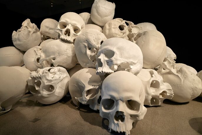White resin casts of a group of oversized human skulls all arranged in close proximity.