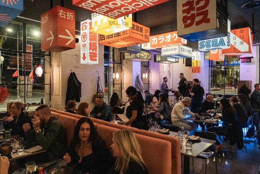 A busy Japanese restaurant with illuminated signage hanging from the ceiling. 