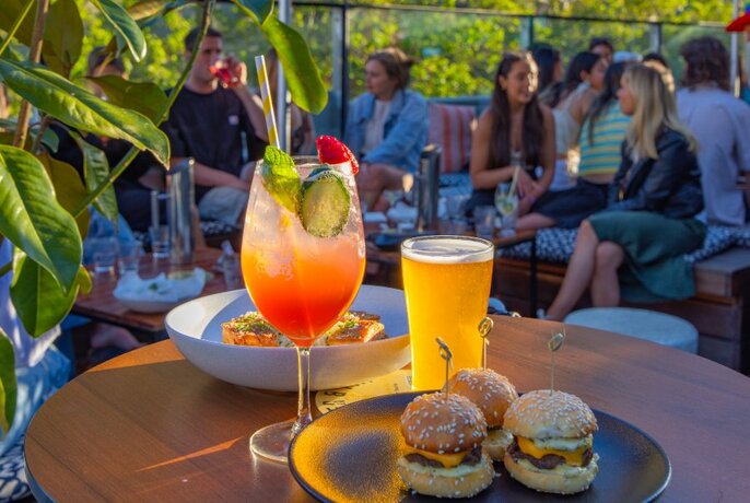 A spritz, beer and sliders on a table on a rooftop bar.