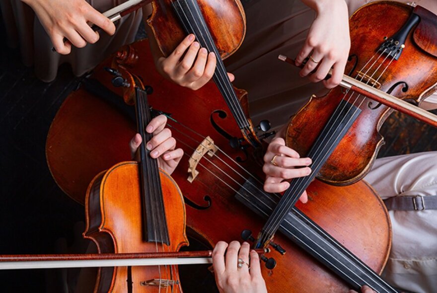 Looking straight down on four stringed instruments and hands playing them, all bunched close together. 