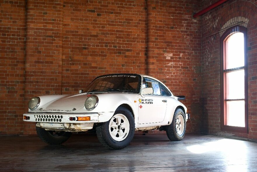 A sporty vintage Porsche with custom details parked next to a redbrick wall.