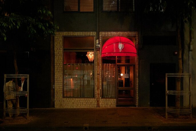 A glowing red street canopy over a dark doorway in a laneway.