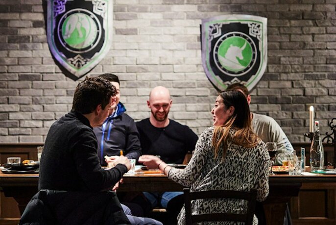 A table of trivia players in a brick-lined gaming room hung with shields.