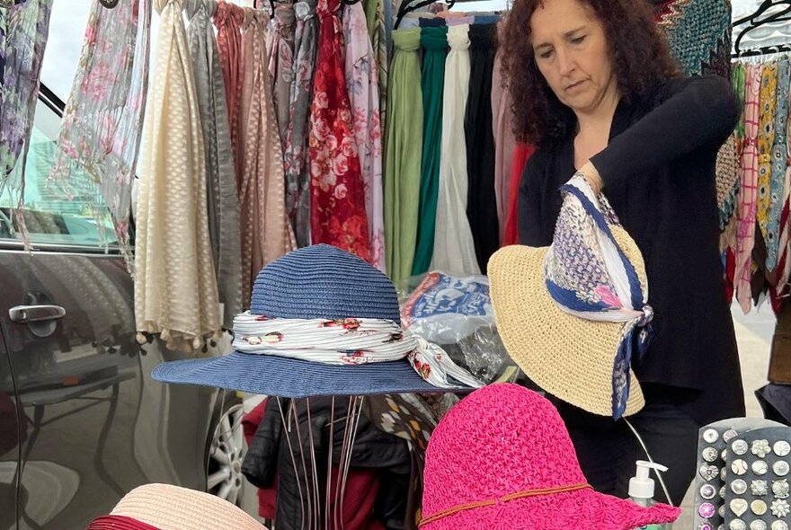 A woman working at a stall with hats and garments. 