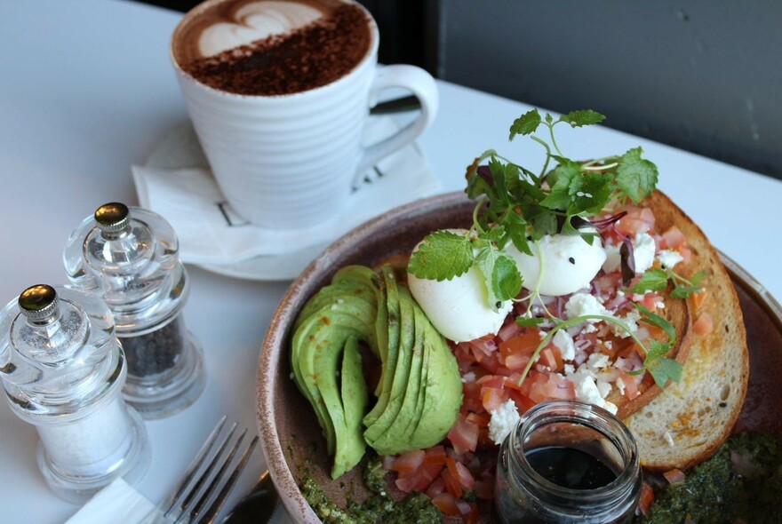 Cappuccino and plate of eggs, avocado and tomato toast.