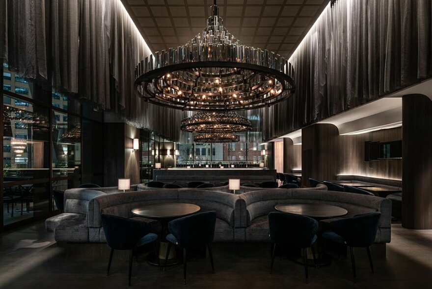 A moody restaurant with grey booths, curtains and a giant chandelier. 