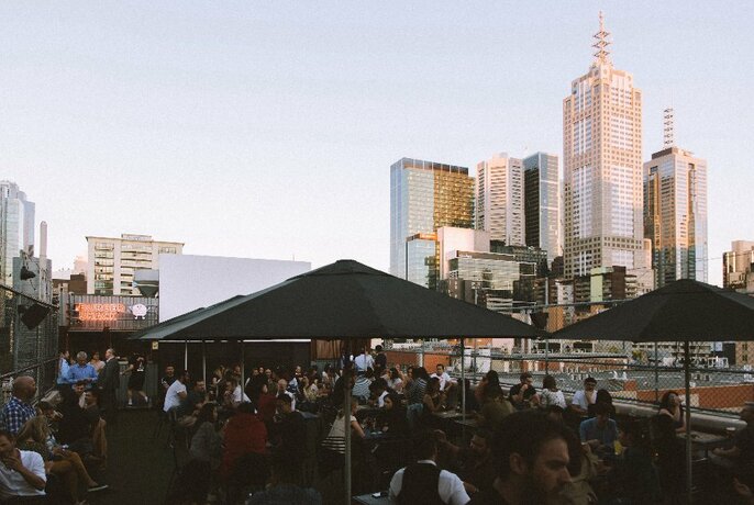 People enjoying drinks at a rooftop bar with cityscape in the background.
