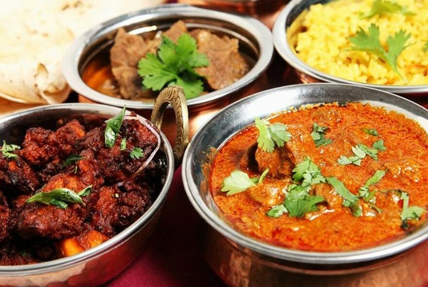 Silver bowls of curries, rice and tandoori meat.
